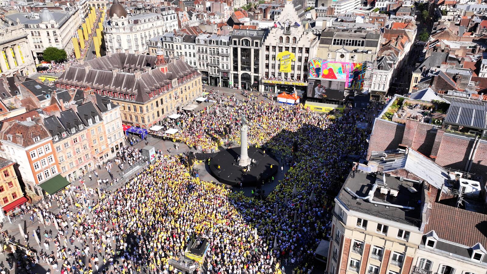 L'image montre la Grand'Place de Lille depuis le ciel, remplie de milliers de personnes habillées de jaune